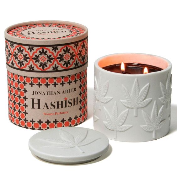 A decorative paper candletube packaging on the left. The packaging has a design that includes words and logo, along with a floral pattern. The candle itself on the right has a leaf motif.