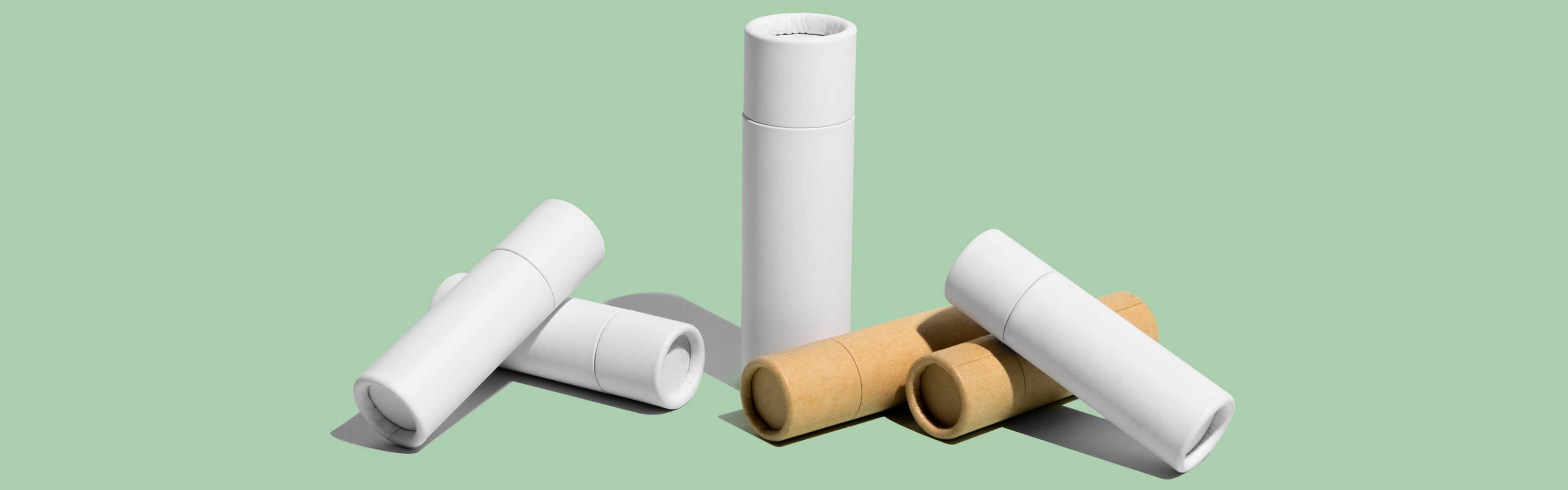 Assorted cylindrical paper tubes in natural cardboard and white colors on a pale green background, indicative of eco-friendly packaging options for cosmetics or personal care products.