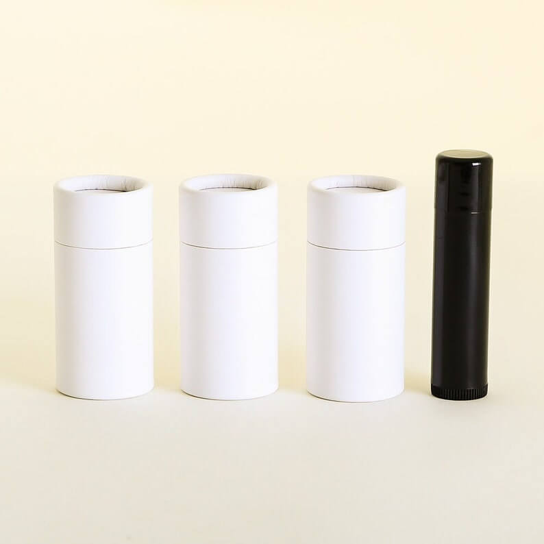 Three closed white cylindrical containers and one black cylindrical container aligned side by side on a pale yellow background.