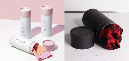 Two cylindrical paper packaging are shown. The first white container with pink accents holds a light pink t-shirt. The second black paper tube contains a red and black checkered t-shirt.