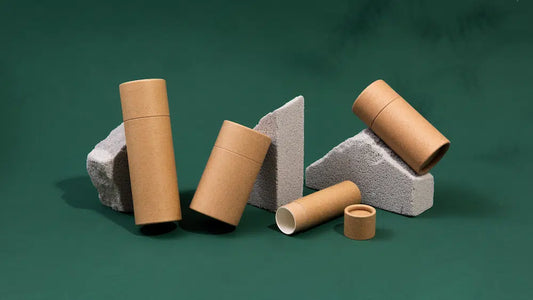 Minimalist brown paper tube packaging displayed on a green background with grey stone props.