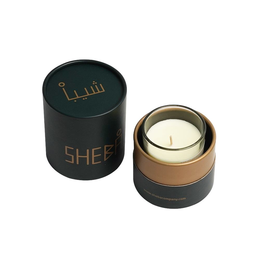 A dark cylindrical container with gold lettering next to its lid, revealing a soy candle with a gold-tone rim on a white surface, suggesting a sophisticated, aromatic accessory.