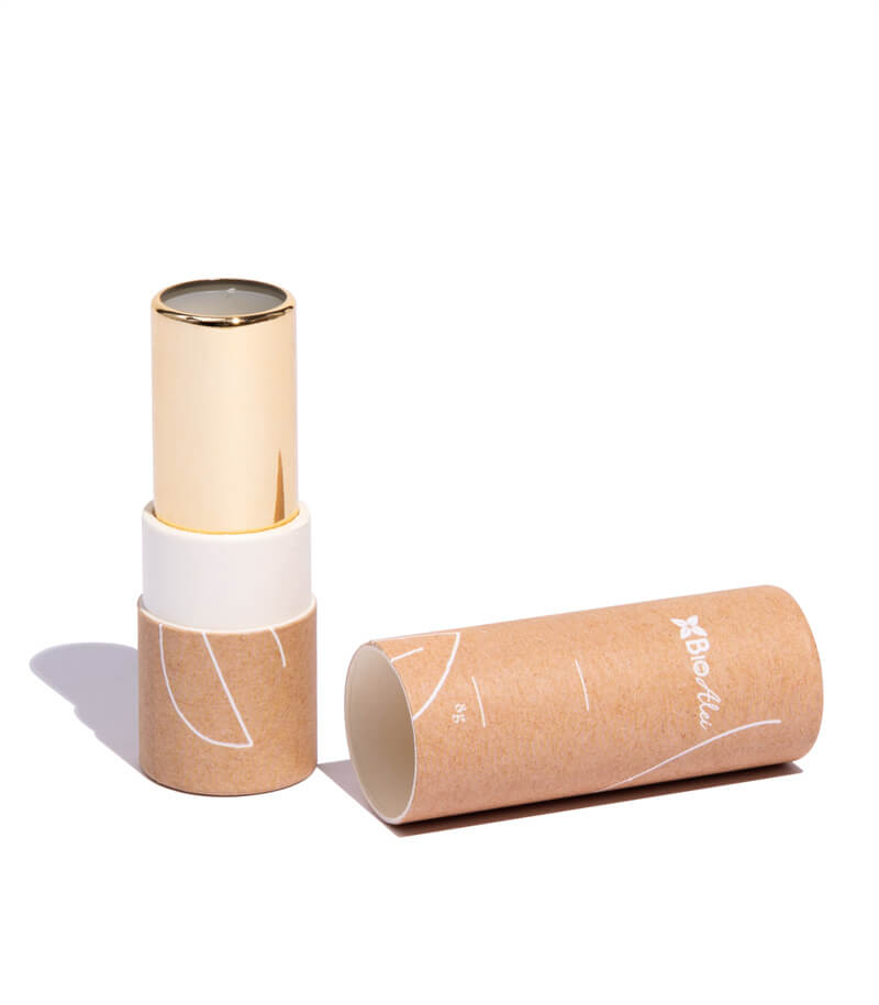 A cylindrical container with a natural brown finish and simple line drawings, next to a golden and white inner tube, all against a stark white background, suggesting sustainable design.