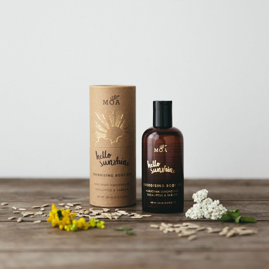 Natural-themed body oil packaging with a cardboard paper tube and a brown glass bottle, both printed with logo and displayed among scattered flower petals, conveying an organic and wholesome aesthetic.