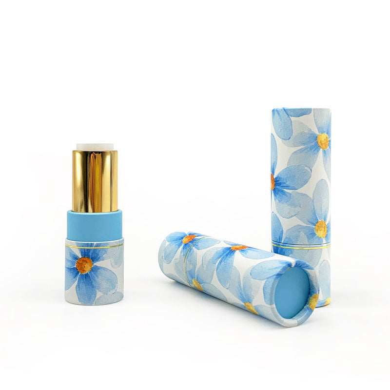 Floral-patterned paper tubes in soft blue, with delicate yellow flowers, are paired with an open lipstick featuring a golden cap and blue base on a white surface.