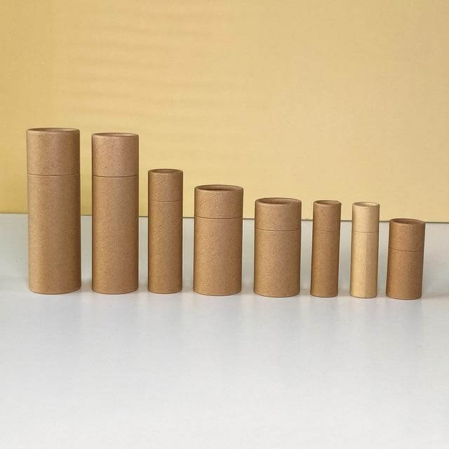 A descending lineup of cylindrical kraft paper tubes arranged from tallest to shortest on a surface, with a contrasting yellow backdrop highlighting their uniform brown tones.