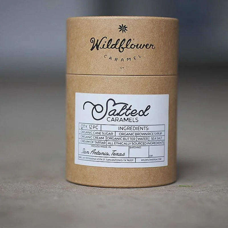 A single kraft paper tube with a white label against a concrete backdrop, suggesting sustainable packaging for gourmet confections.