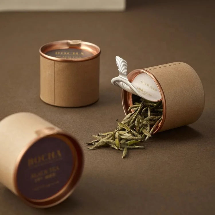 Three open cylindrical containers on a surface, with one spilling loose leaf tea, and all featuring copper-colored lids and eco-friendly design.