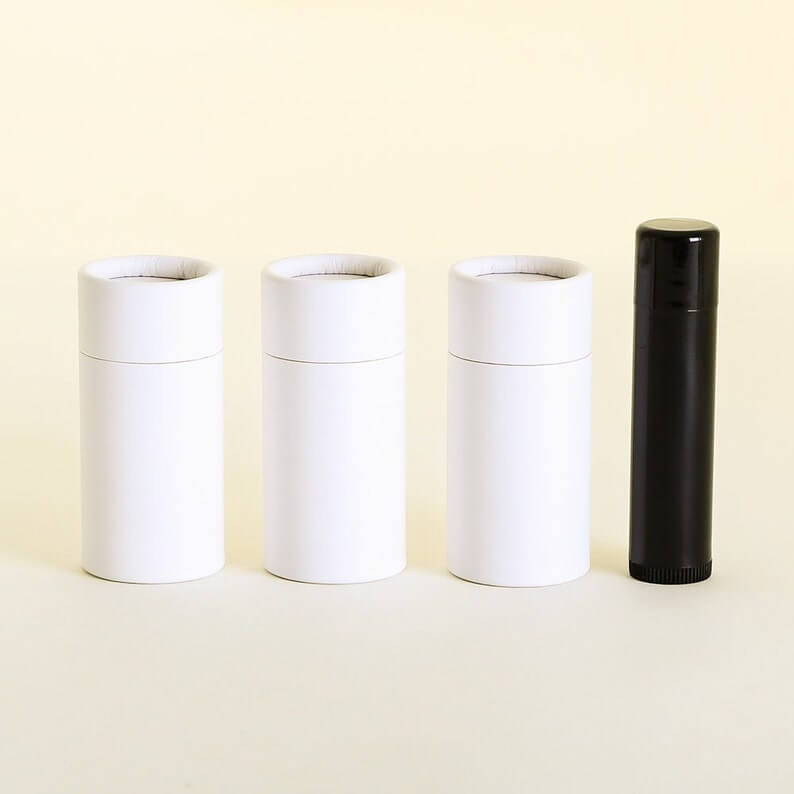 Three closed white cylindrical containers and one black cylindrical container aligned side by side on a pale yellow background.