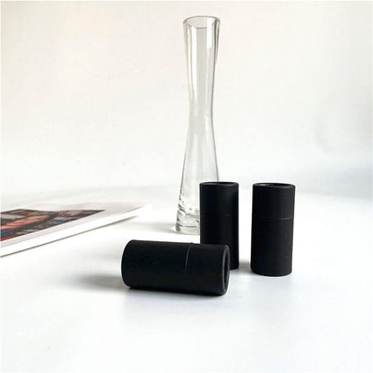 Three 15ml black cylindrical paper tubes on a white surface, with a clear glass vase and a magazine in the background.