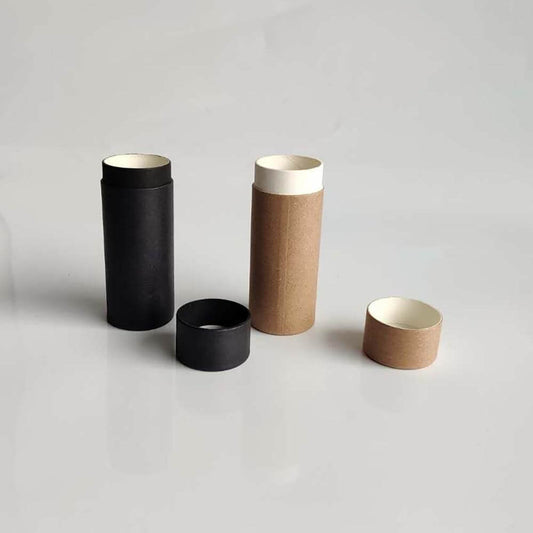 Two standing paper tubes, one black and one brown, next to their respective lids, with the black lid detached, all placed against a neutral grey background, suggesting simplicity and eco-friendly packaging.