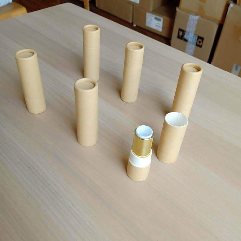 Several pale beige paper tubes are standing vertically on a wooden surface, with two horizontally placed in the foreground showing a metallic gold-colored interior.