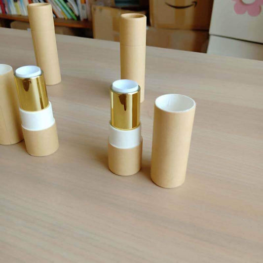 Several pale beige paper tubes are standing vertically on a wooden surface, with two horizontally placed in the foreground showing a metallic gold-colored interior.